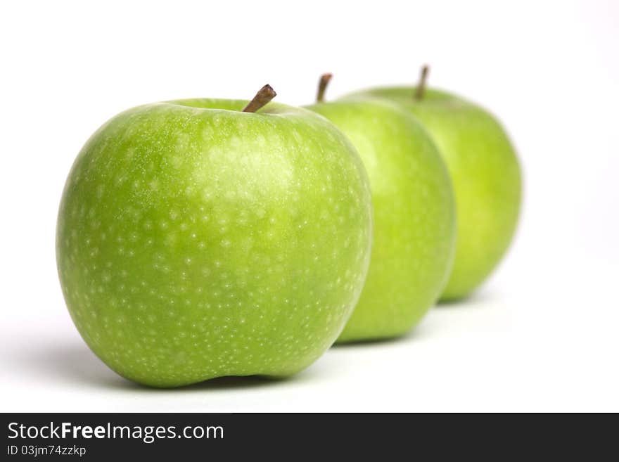 A row of green apples with stalks. A row of green apples with stalks