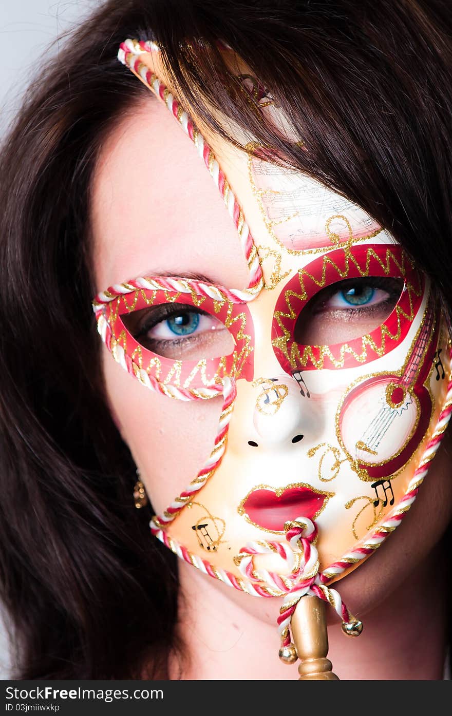 Beautiful young brunette haired, blue eyed model dressed in gold with colorful red and gold venetian carnival face mask. Beautiful young brunette haired, blue eyed model dressed in gold with colorful red and gold venetian carnival face mask