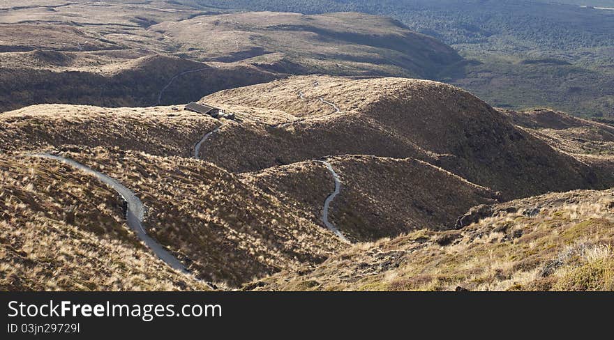 Twisting hilly track from mountain down to hut on sunset. Twisting hilly track from mountain down to hut on sunset