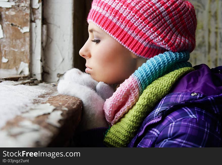 A beautiful woman in warm clothes standing near the window.