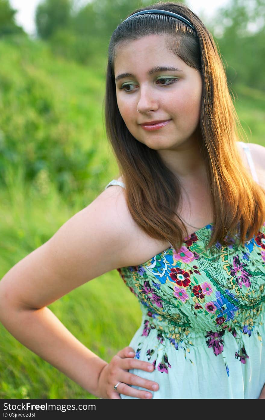 The portrait of young smiling girl in light dress on a the summer green background