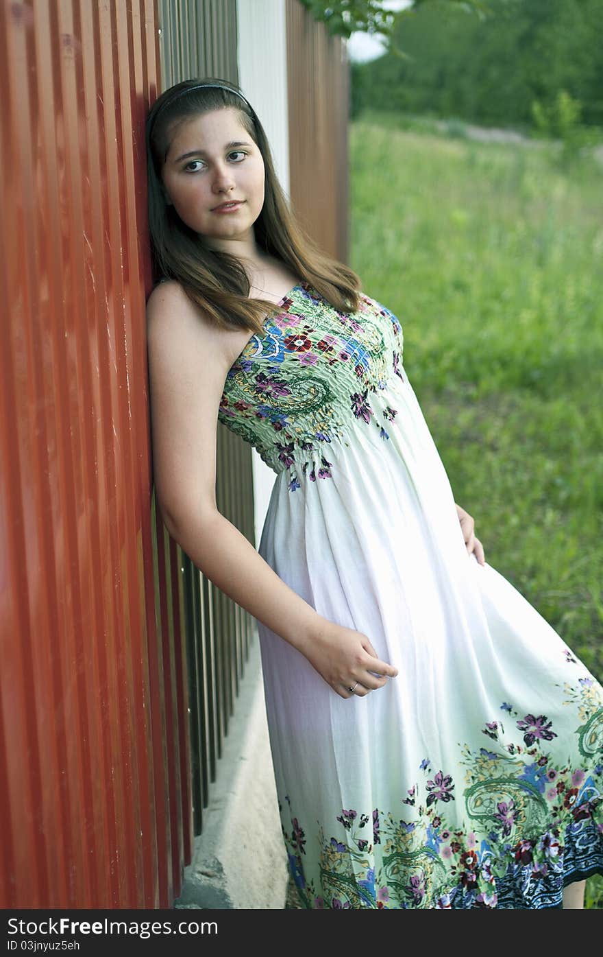 Young beautiful girl in light dress against metal fence