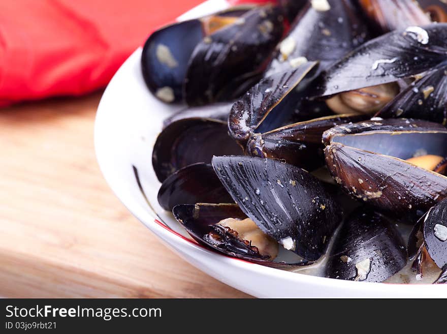 Close up picture of mussels in the bowl on wooden board.