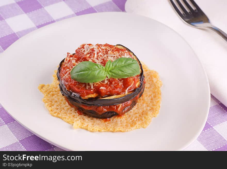 Parmigiana di melanzane over a cheese disk decorated with fresh basil. Parmigiana di melanzane over a cheese disk decorated with fresh basil