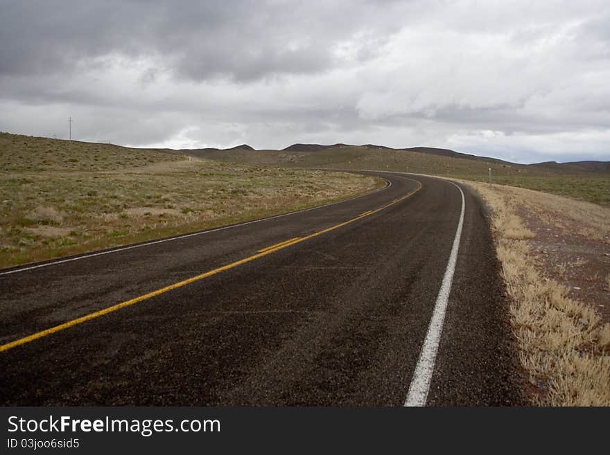 A highway curves through the desert in Nevada, beneath a cloudy sky. A highway curves through the desert in Nevada, beneath a cloudy sky.