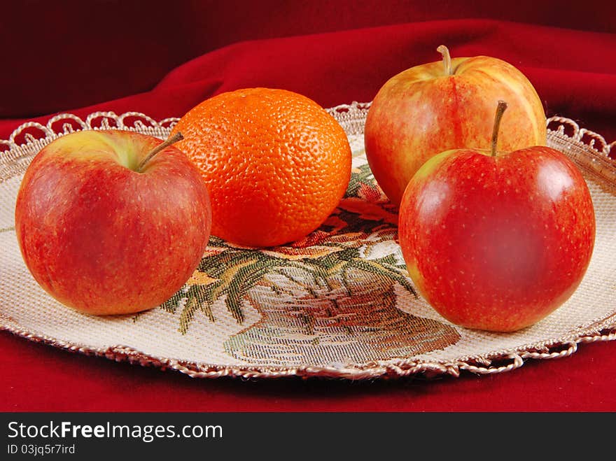 Three apples and one orange on serviette. Red studio background