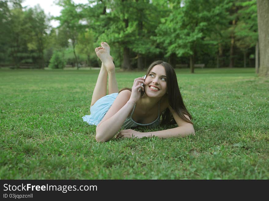 Smiling woman lying on a green meadow and talking on the mobile phone. Smiling woman lying on a green meadow and talking on the mobile phone