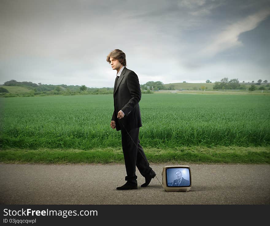 Young businessman walking on a countryside road and carrying a television. Young businessman walking on a countryside road and carrying a television