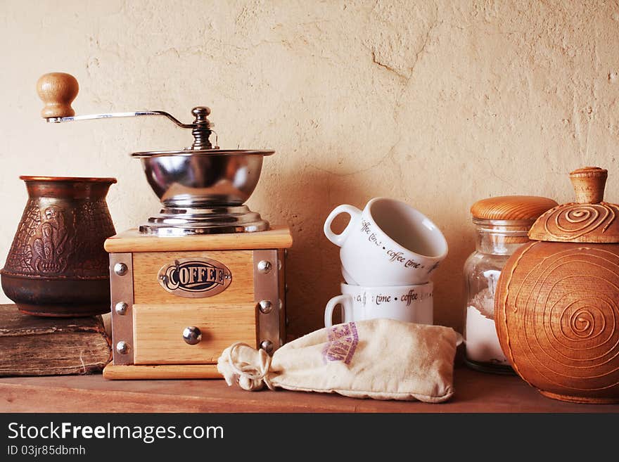 Coffee still life (grinder, cup, a turk, a bag of beans, a jar) against the background of an old wall