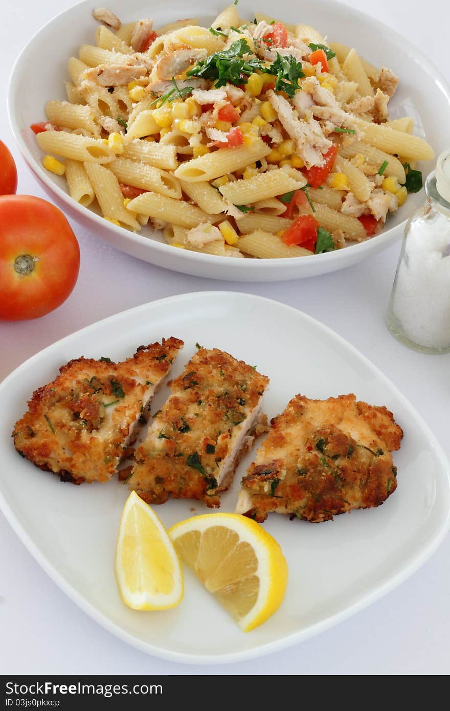 A plate of Chicken Milanese with lemon wedges and a plate of chicken pasta. A plate of Chicken Milanese with lemon wedges and a plate of chicken pasta