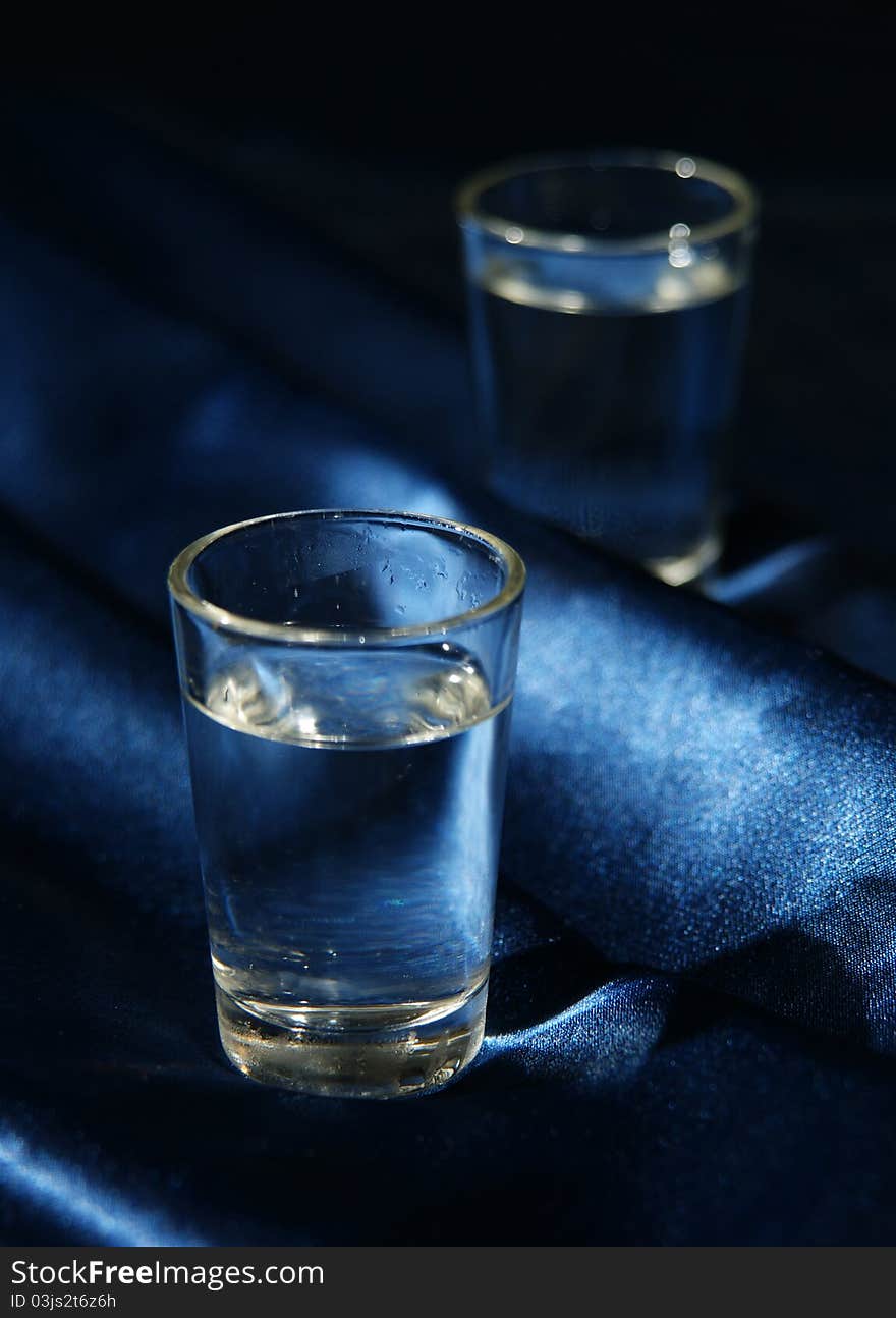 Two glasses with water or spirits on dark blue cloth make a cold and intimate composition. Two glasses with water or spirits on dark blue cloth make a cold and intimate composition