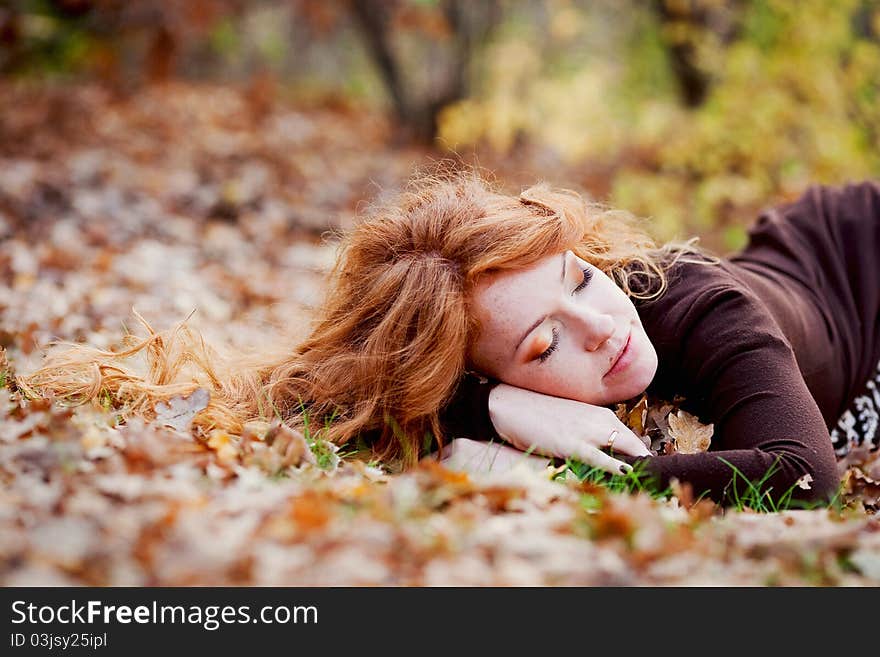 The red-haired girl in autumn leaves outdoor shot