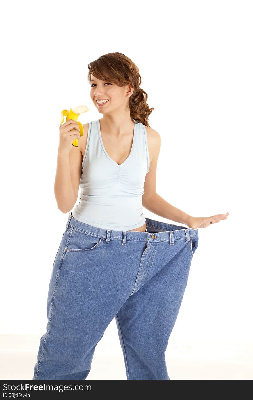 A woman holding out her big pants happy with how she lost weight, as she is holding a banana. A woman holding out her big pants happy with how she lost weight, as she is holding a banana.