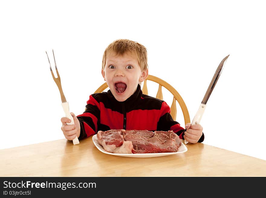 A young boy with a happy expression on his face with a large steak on his plate holding a big knife and big fork. A young boy with a happy expression on his face with a large steak on his plate holding a big knife and big fork.