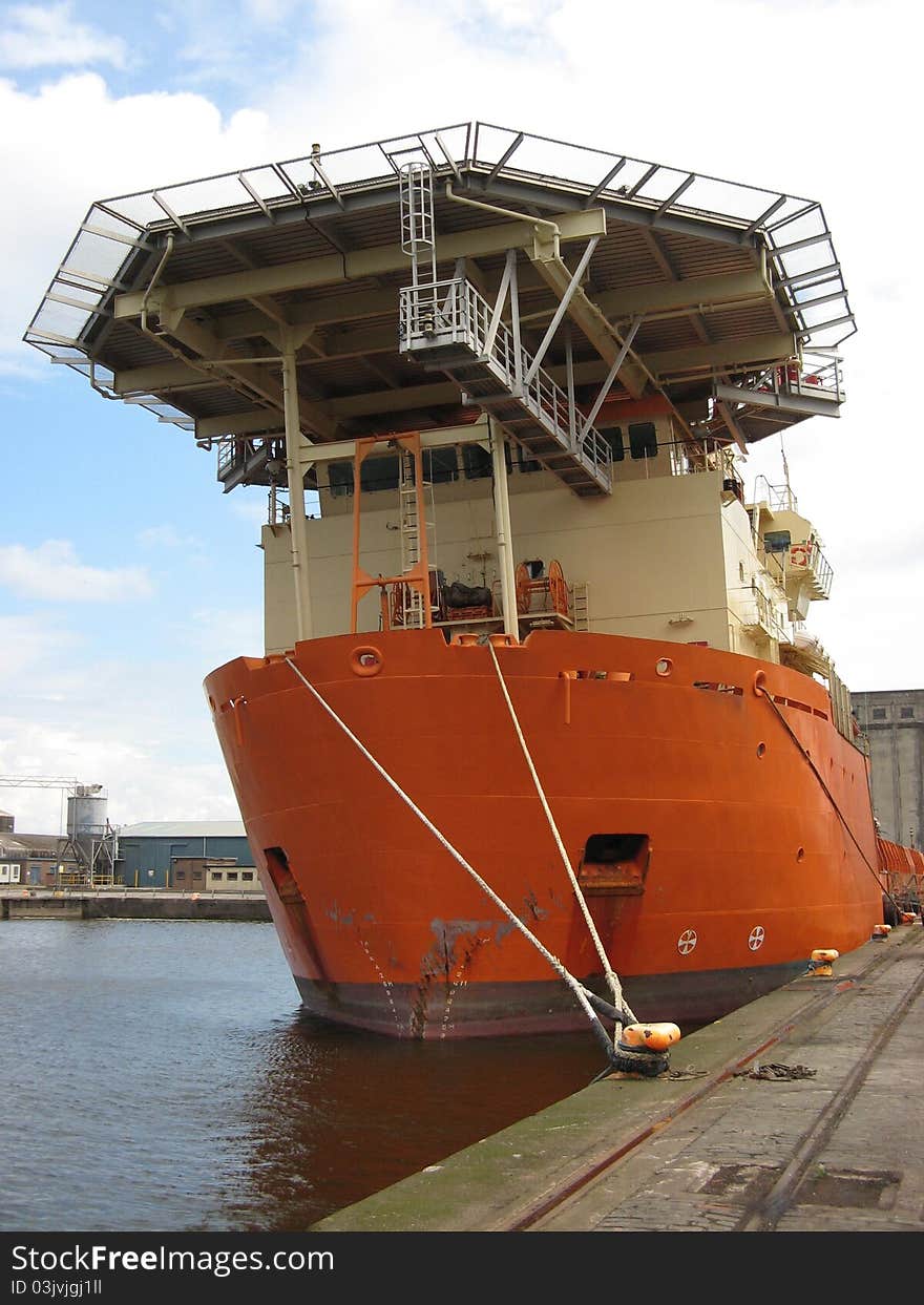 An orange offshore support vessel moored to a quay. An orange offshore support vessel moored to a quay