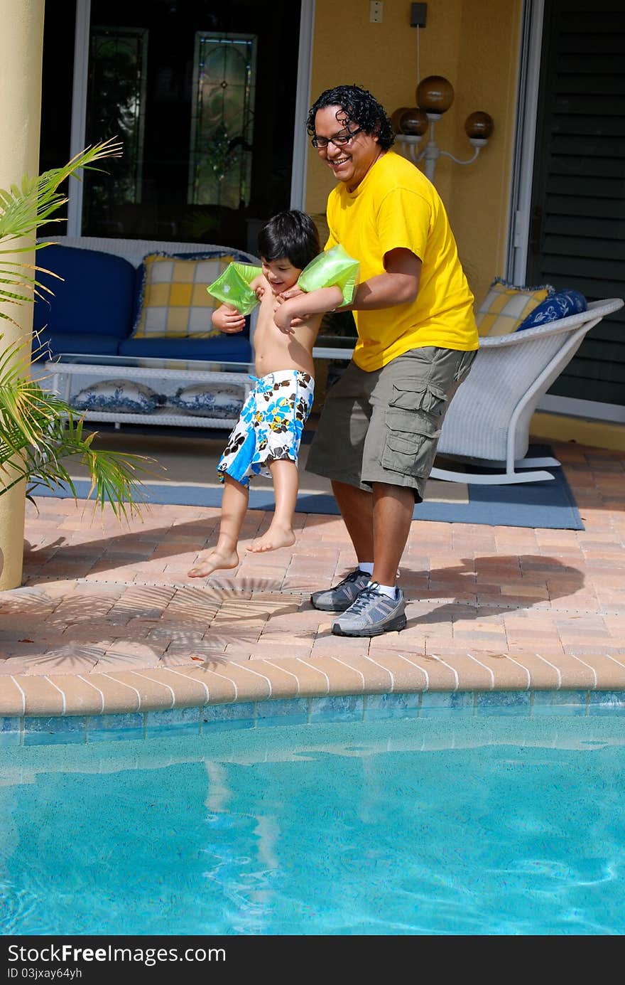 A Hispanic father throws his son into the pool. A Hispanic father throws his son into the pool