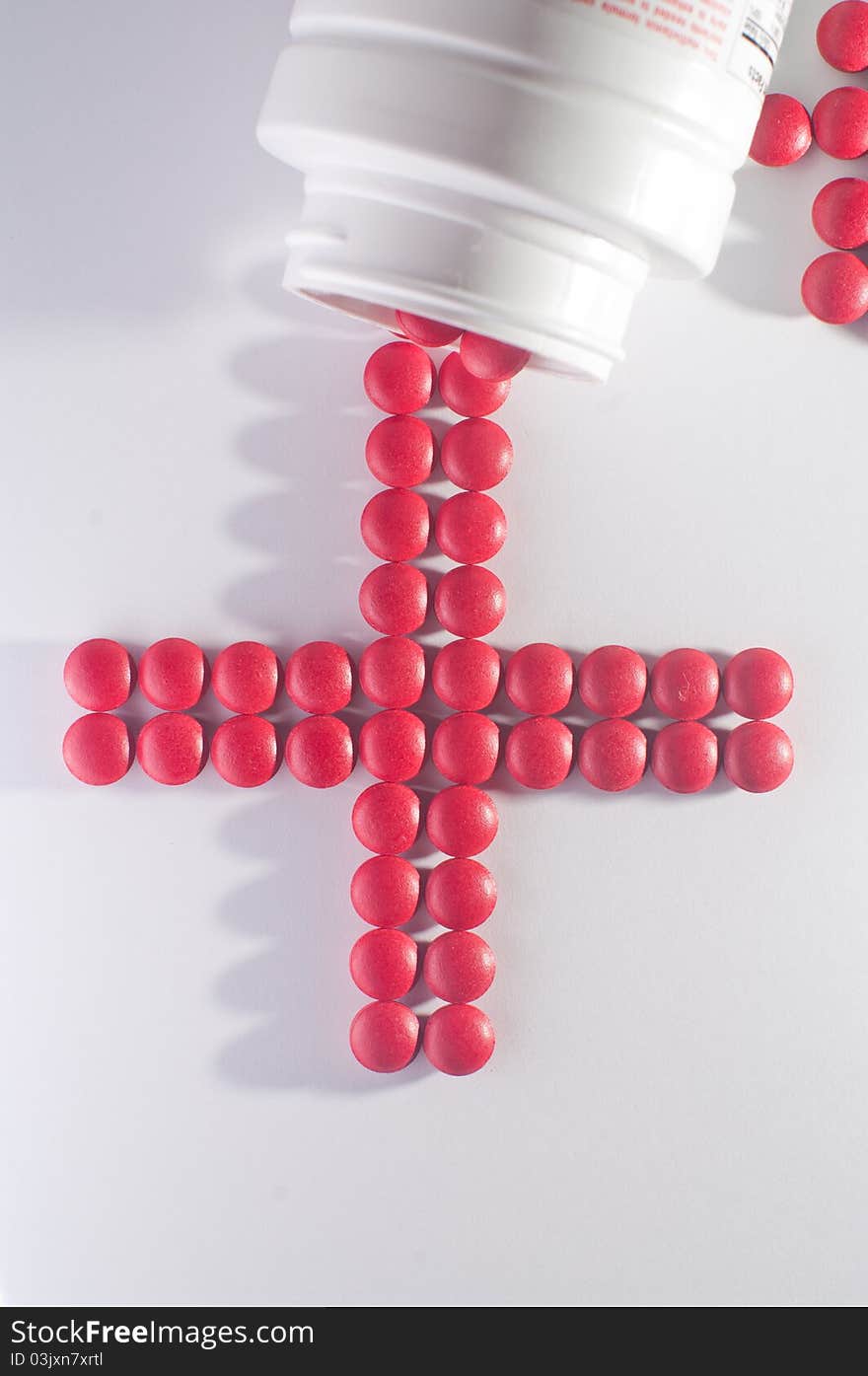 A pile of red pills scattered in the shape of cross on a white background