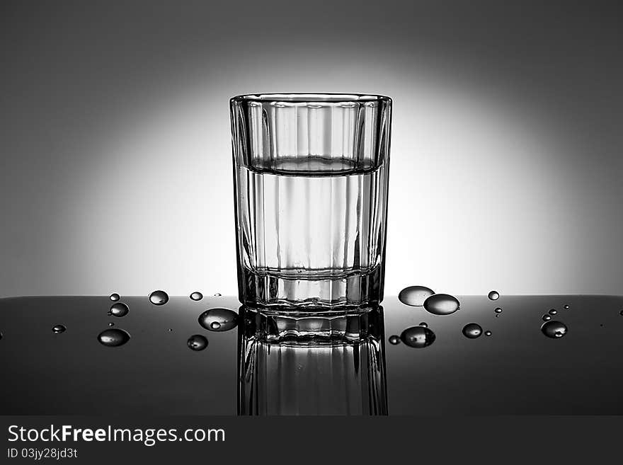 A faceted glass with water drops near it in spot of light.