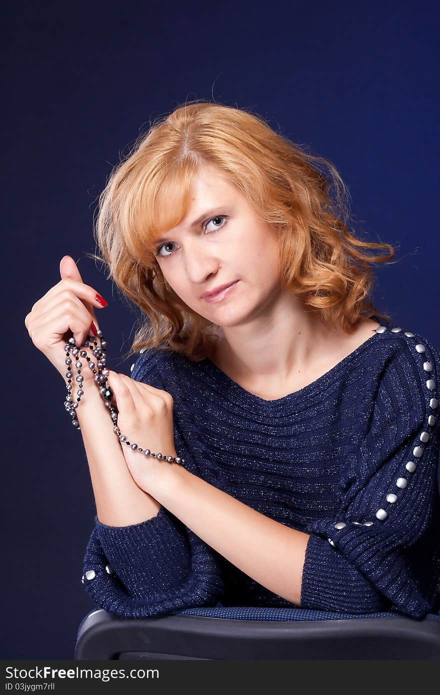 Red-haired girl in a blue blouse with a blue background with beads. Red-haired girl in a blue blouse with a blue background with beads