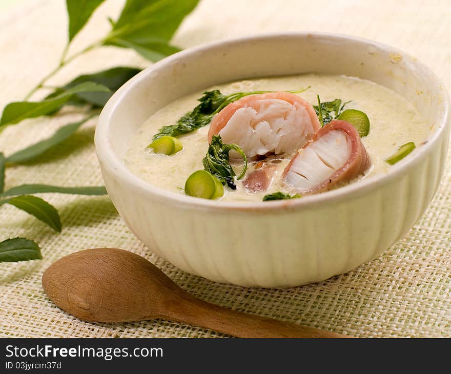 A bowl of asparagus creamy soup with fish, bacon and parsley