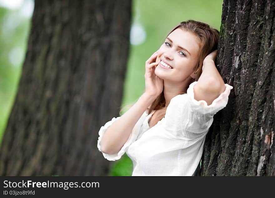 Happy young woman standing near the tree in the park on a warm summer day. Happy young woman standing near the tree in the park on a warm summer day