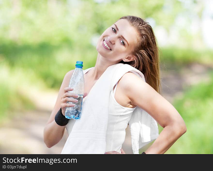 Beautiful young  sporty woman running in the park on a warm summer day and drinking water