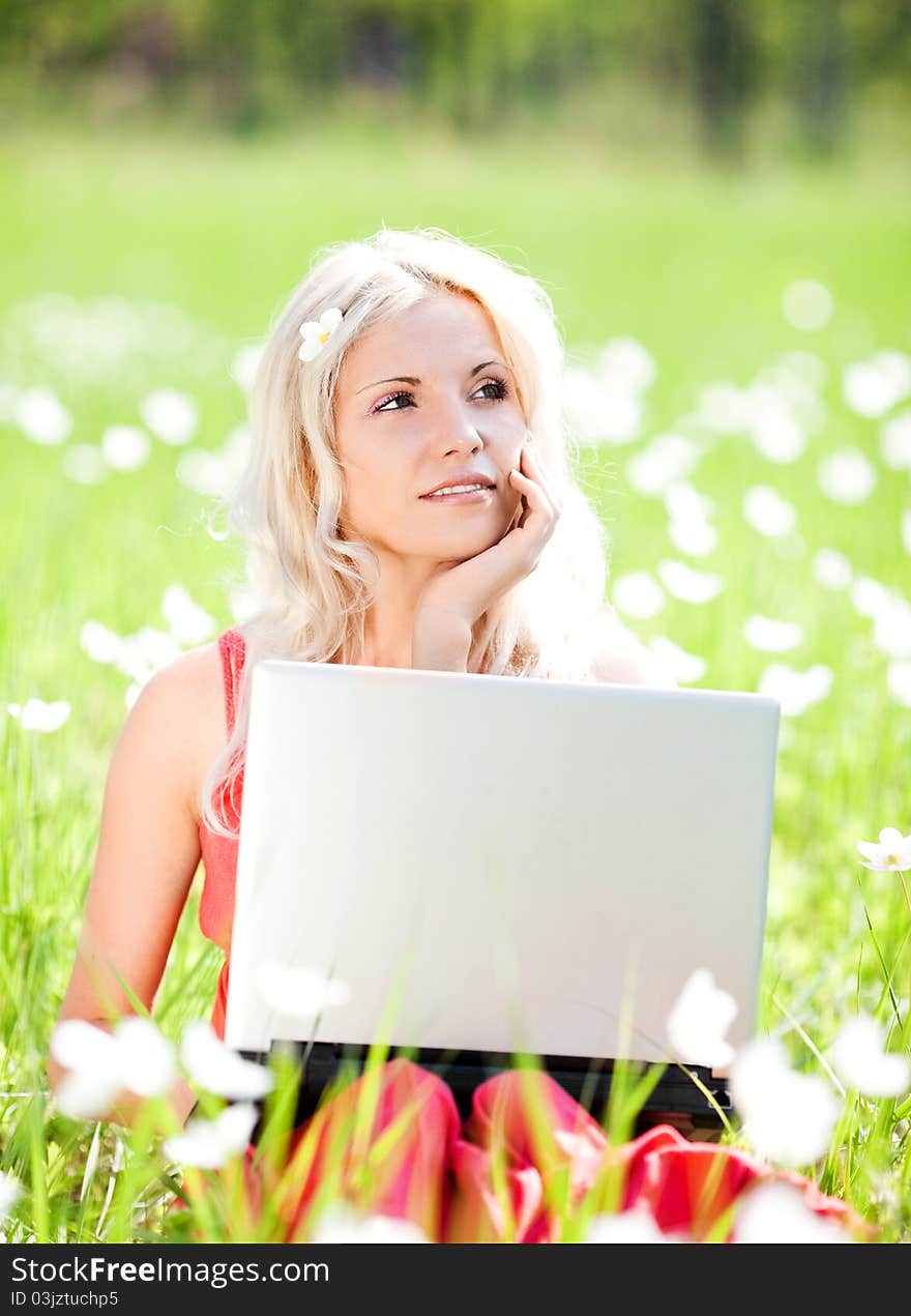 Beautiful young blond woman with a laptop  in the park  on a warm summer day