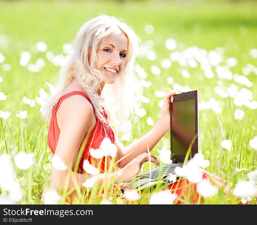 Beautiful young blond woman with a laptop  in the park  on a warm summer day