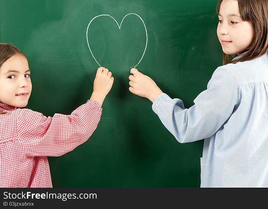 Two girls drawing a heart on a green blackboard. Two girls drawing a heart on a green blackboard