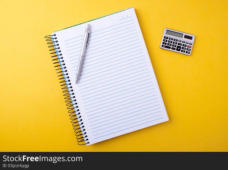 Ballpoint pen on a copybook and calculator on a yellow background. Ballpoint pen on a copybook and calculator on a yellow background