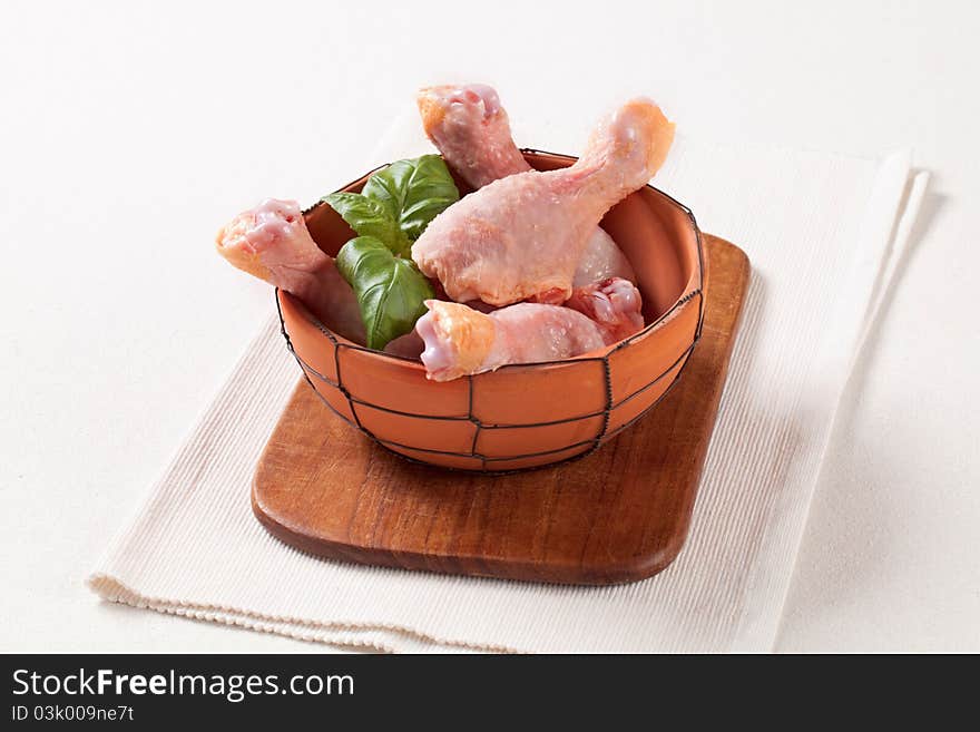 Raw chicken drumsticks in a terracotta bowl