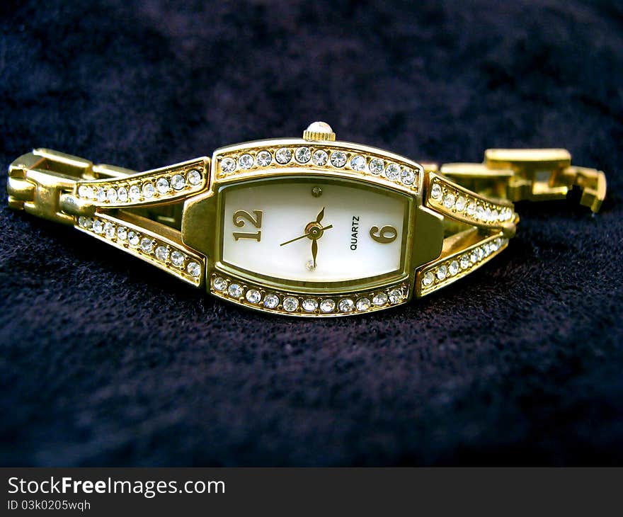 A golden ladies watch on top of black seude material.