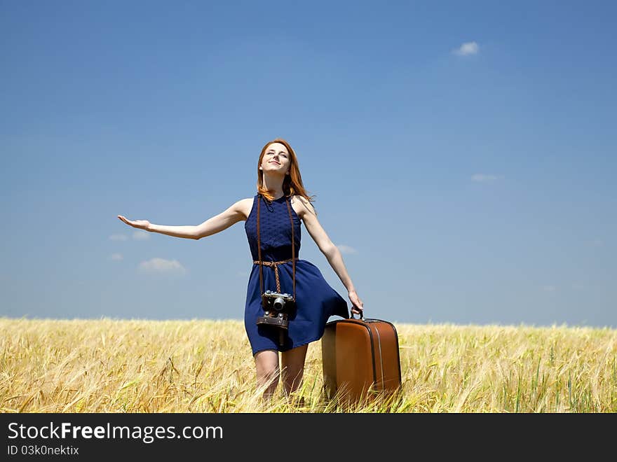 Girl with suitcase at spring wheat field.