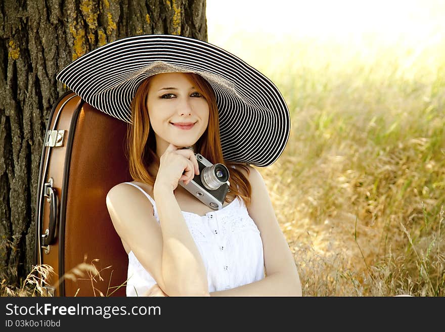 Redhead girl sitting near tree with vintage camera.