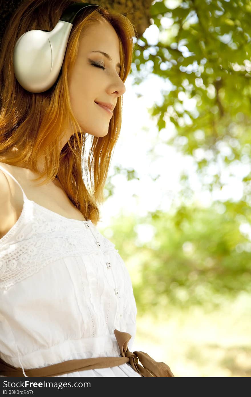 Redhead girl with headphones at garden.