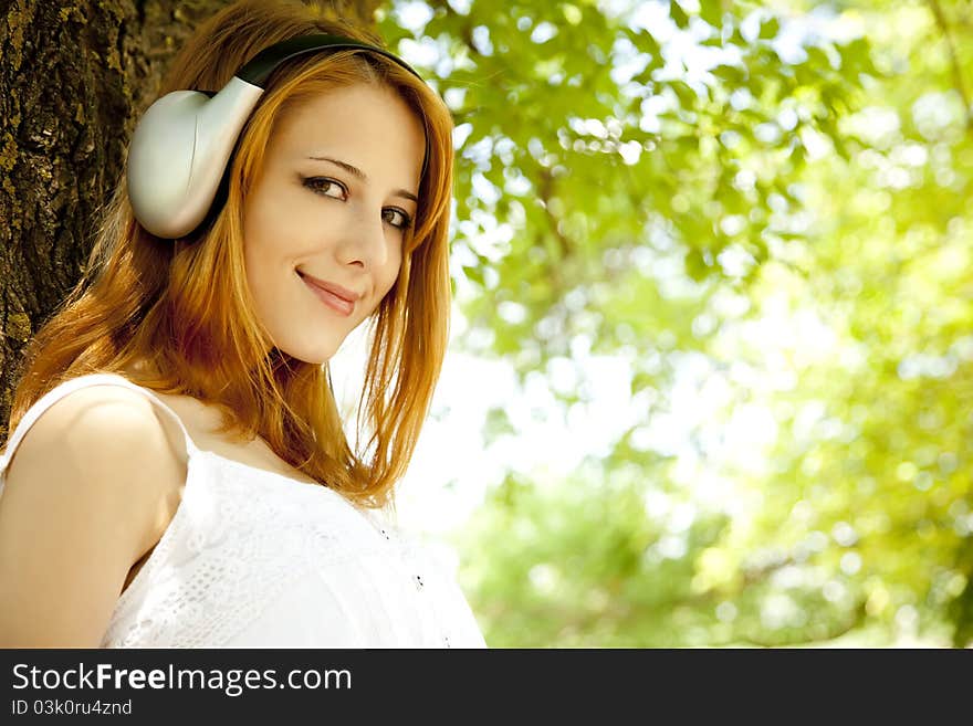 Redhead girl with headphones at garden.