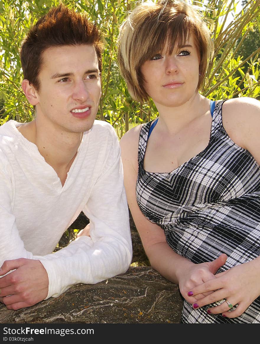 TwoTeen  friends, young man with  young women leaning on a log outside. Both are looking off into the distance. Backlit by sun with park trees in background. TwoTeen  friends, young man with  young women leaning on a log outside. Both are looking off into the distance. Backlit by sun with park trees in background