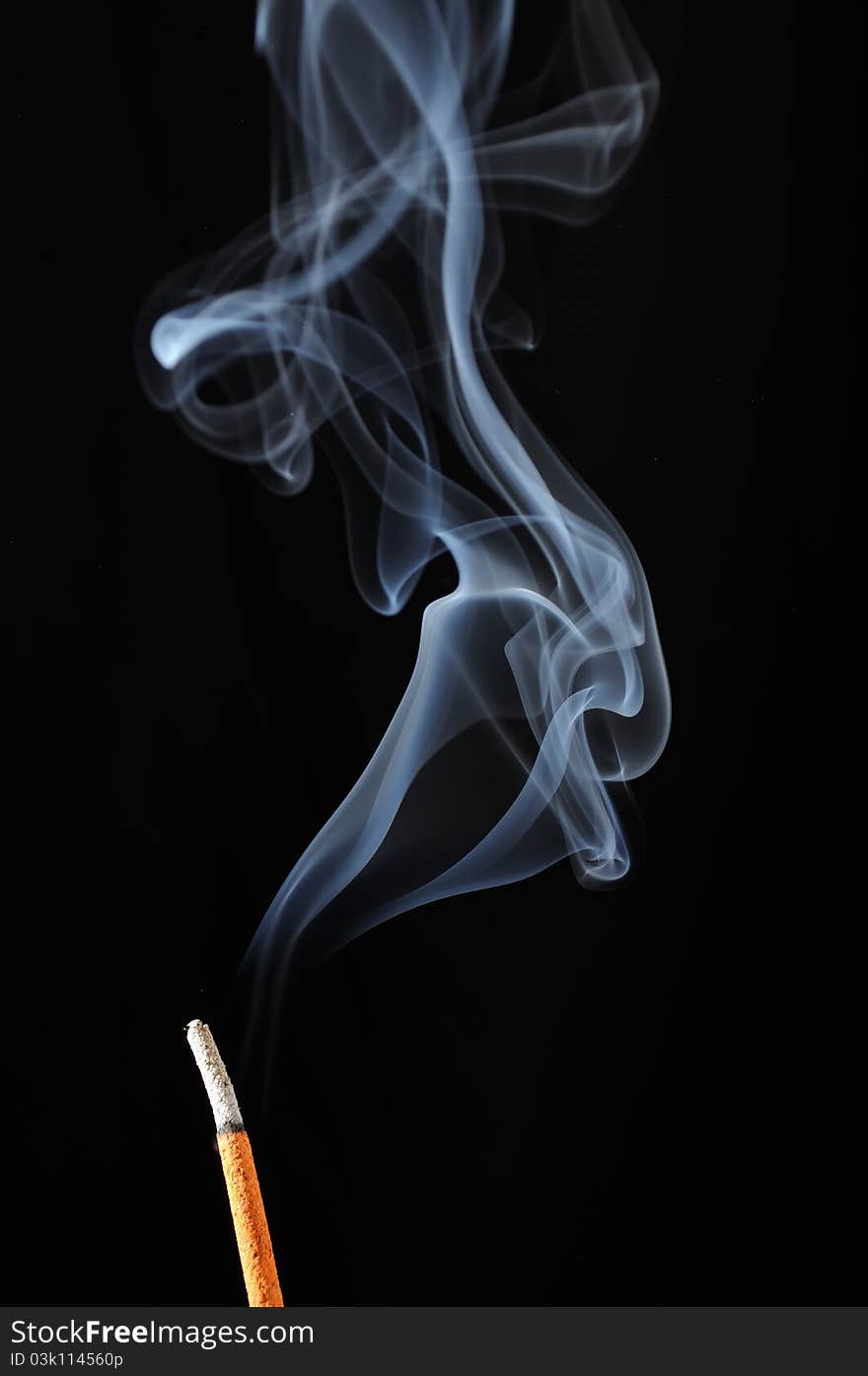 A burning incense stick with smoke on a black background