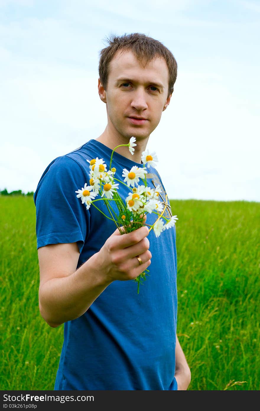 The young man with camomiles on green meadow