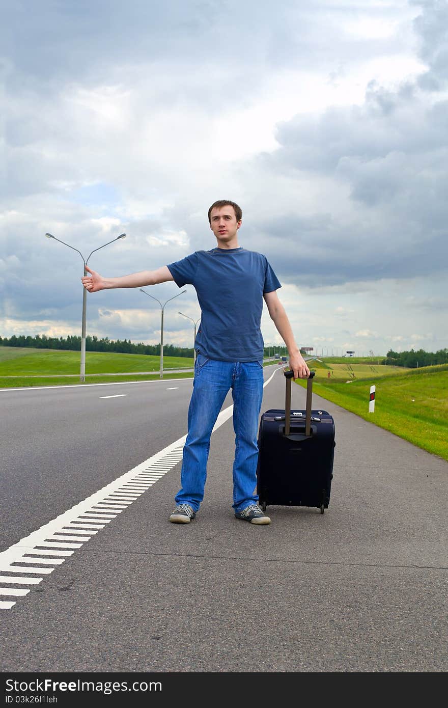 The young man pending on road with suitcase