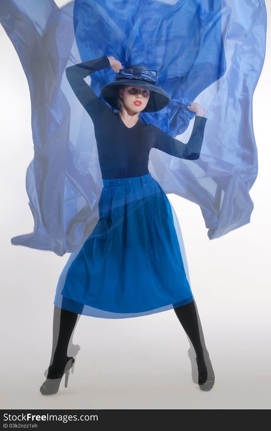 Woman in a dynamic pose, dressed in a blue skirt and a classic hat with a big bow, holding a piece of blue cloth flying. Woman in a dynamic pose, dressed in a blue skirt and a classic hat with a big bow, holding a piece of blue cloth flying.