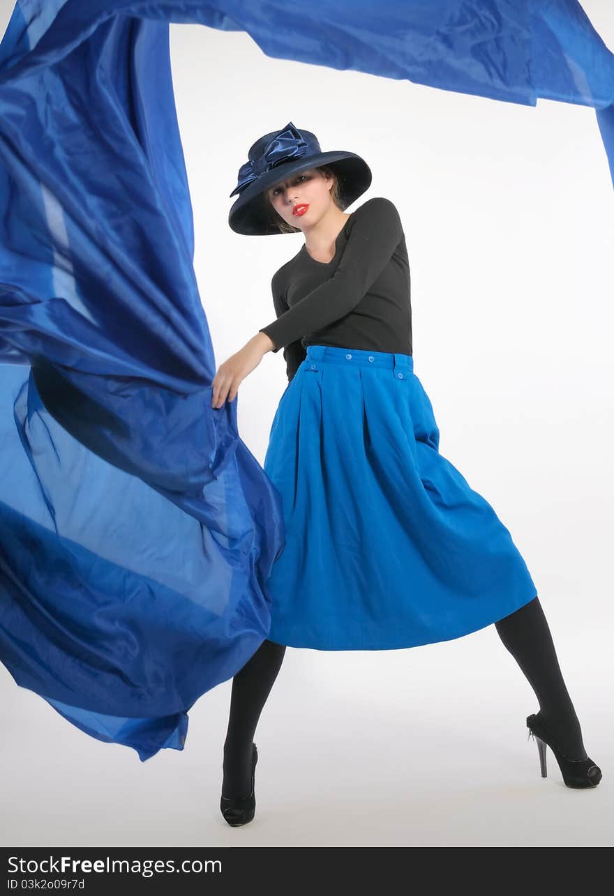 Woman in a dynamic pose, dressed in a blue skirt and a classic hat with a big bow, holding a piece of blue cloth flying. Woman in a dynamic pose, dressed in a blue skirt and a classic hat with a big bow, holding a piece of blue cloth flying.