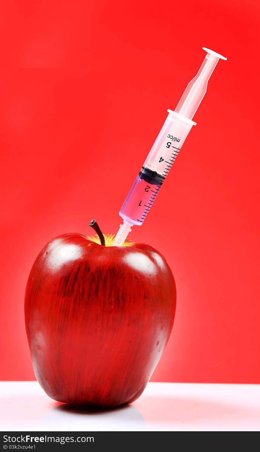 A red apple being injected with syringe containing colour fluid. A red apple being injected with syringe containing colour fluid.