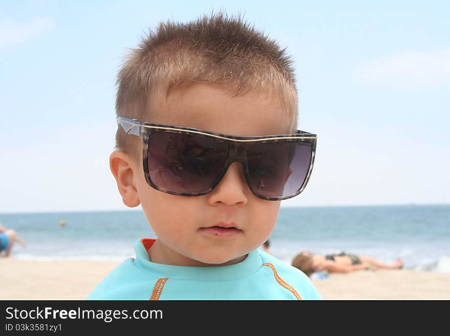 Male todler sitting on the beach wearing sunglasses. Male todler sitting on the beach wearing sunglasses.