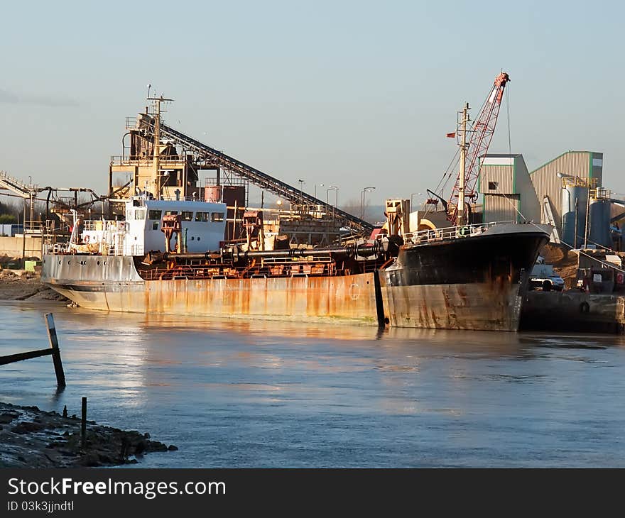 A dredger ship delivers gravel at a port on a winter afternoon. A dredger ship delivers gravel at a port on a winter afternoon.