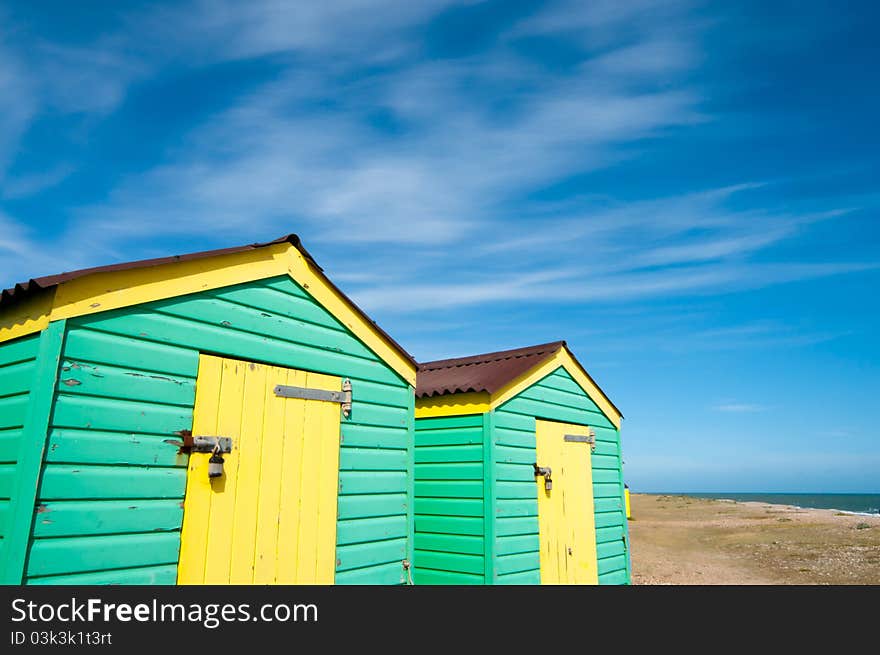 Green and yellow beach huts against an empty beach in England. Green and yellow beach huts against an empty beach in England.