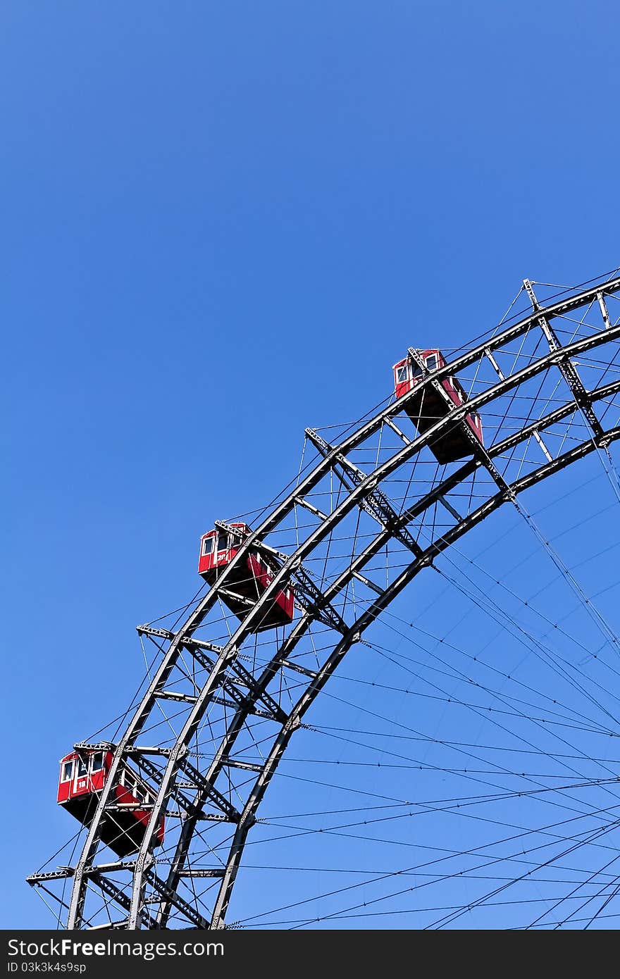 A segment of Vienna's ferris wheel with three cabins against the blue sky