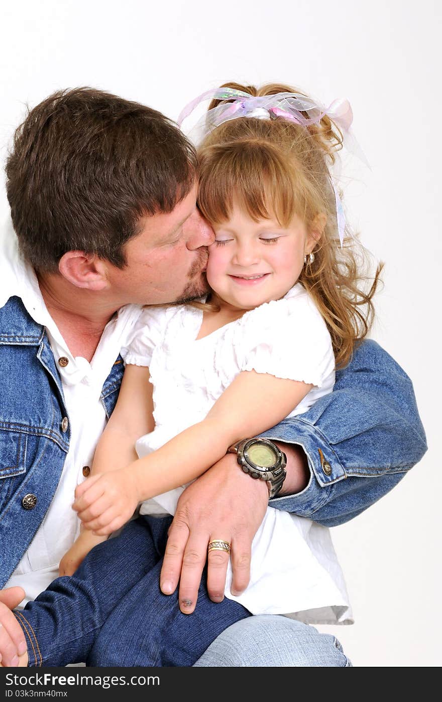 Young father dressed in jeans and toddler girl dressed in white hugging and smiling lovingly while kissing. Young father dressed in jeans and toddler girl dressed in white hugging and smiling lovingly while kissing