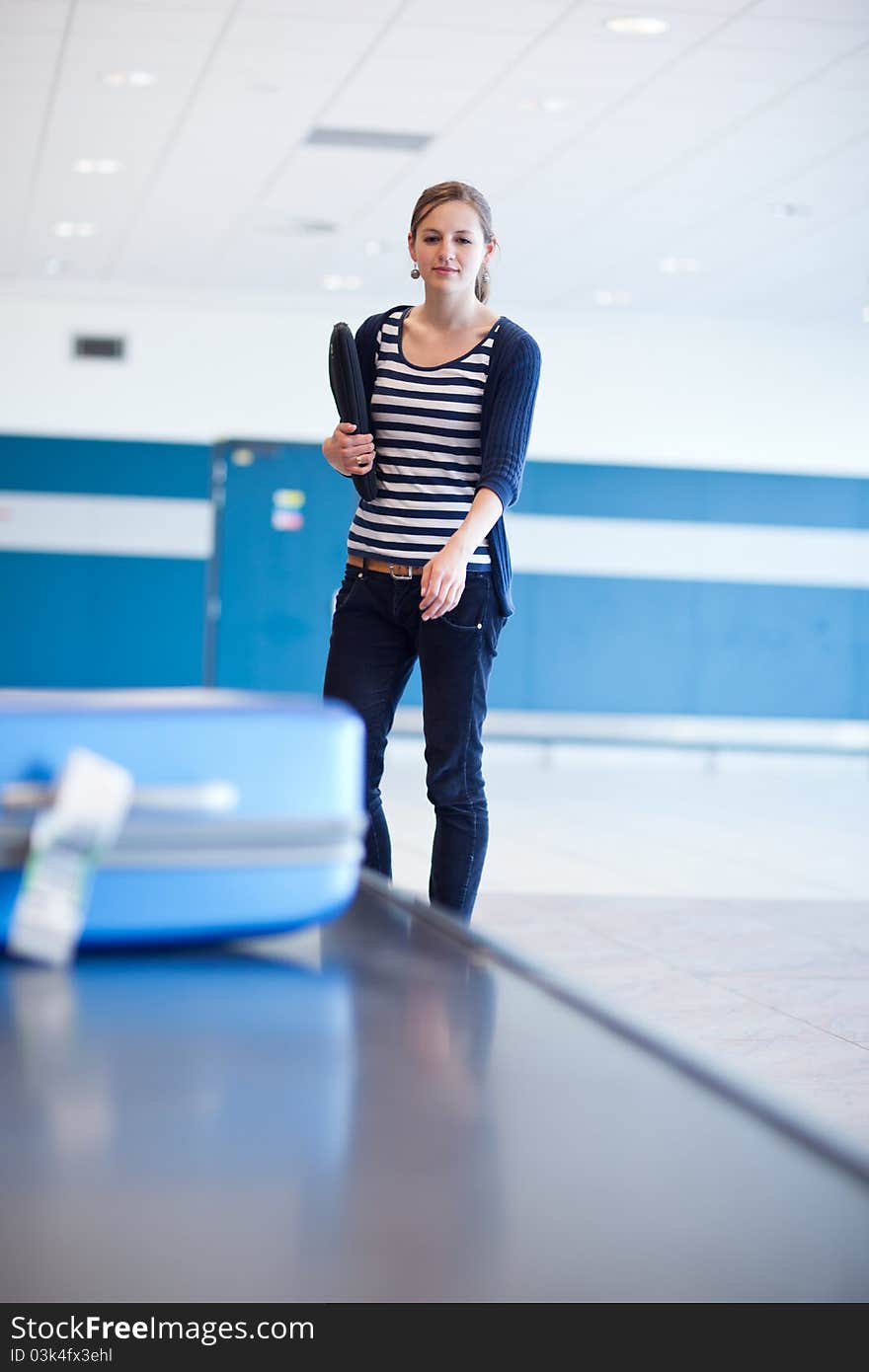 Baggage reclaim at the airport - pretty young woman taking her suitcase off the baggage carousel (color toned image)