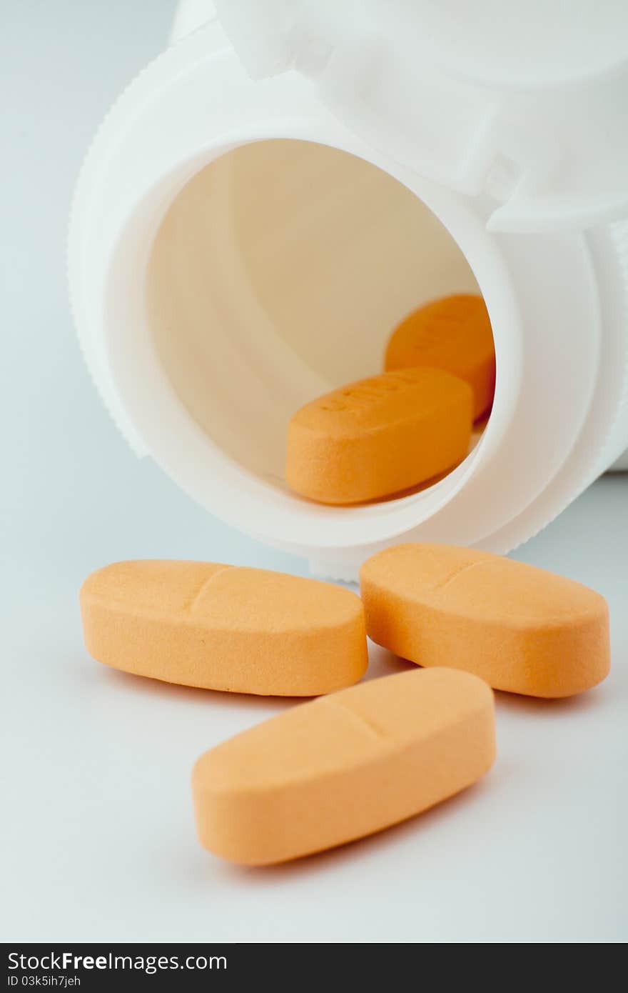 Heap of orange tablets with a jar on white